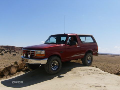 1993 Ford Bronco - Red 1993 Ford Bronco on an off-road trail under a clear blue sky.