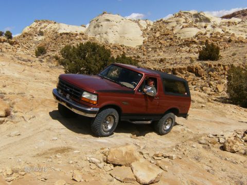 1993 Ford Bronco - A 1993 Ford Bronco navigates a , rocky terrain under a clear blue sky.
