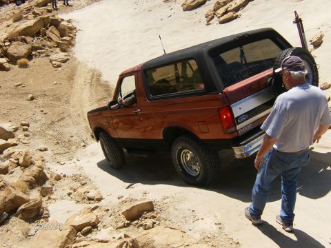 1993 Ford Bronco - A man stands near an orange and black Ford Bronco navigating a rocky, off-road trail.