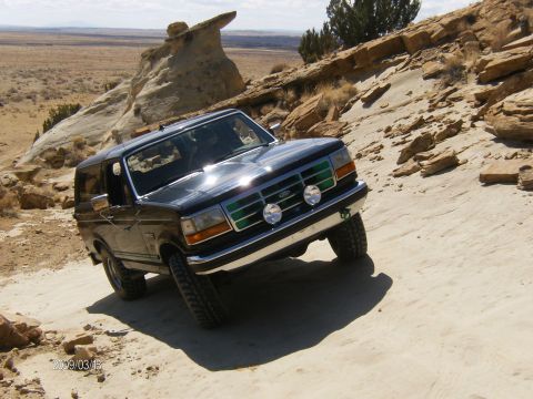 1993 Ford Bronco - Black 1993 Ford Bronco navigates a steep, sandy, and rocky off-road path in a desert landscape.
