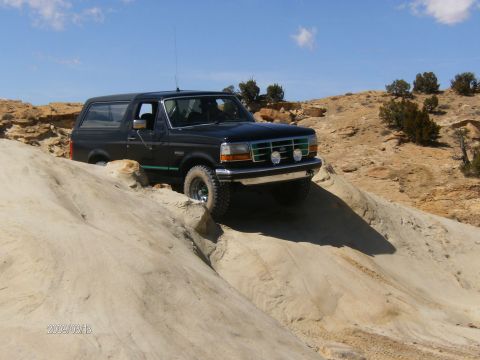 1993 Ford Bronco - A black Ford Bronco navigates a challenging off-road trail with sandy and rocky terrain.