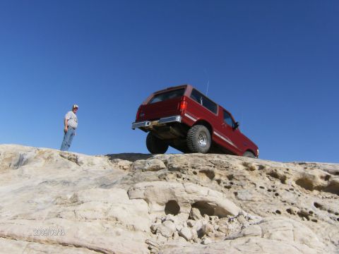 1993 Ford Bronco - A red SUV navigates a rocky landscape under a clear blue sky.