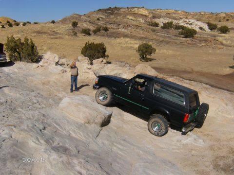 1993 Ford Bronco - A black 1993 Ford Bronco navigates a challenging rocky trail under a clear blue sky.