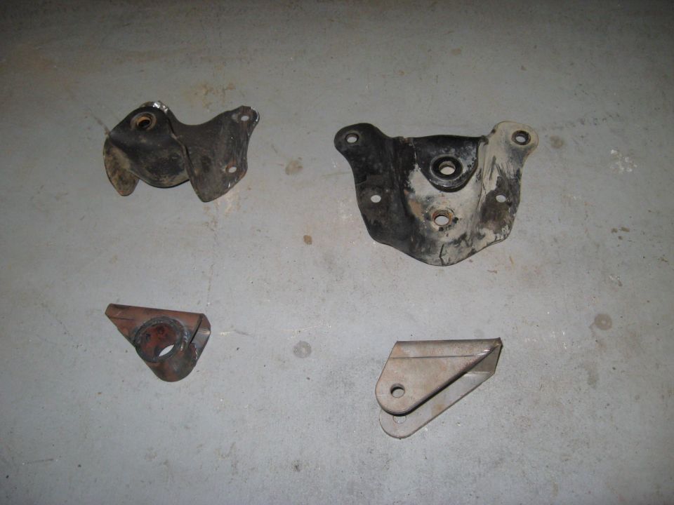 Four metal brackets, likely suspension or engine mounts, on a concrete floor