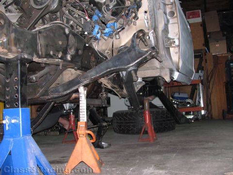 1990 Ford Bronco - vehicle on blue and red jack stands with a long fabricated suspension arm reaching to a mounted off-road tire.