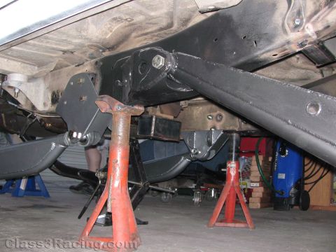 1990 Ford Bronco - underside of a vehicle on orange jack stands, showing fabricated rear suspension trailing arms and brackets.