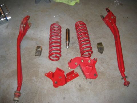 1909 Ford Bronco - Various red suspension parts, including coil springs and control arms, are displayed on a concrete surface.