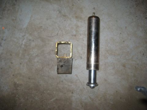 1909 Ford Bronco - Two automotive parts, a shock absorber and a hitch receiver component, lie on a concrete surface.