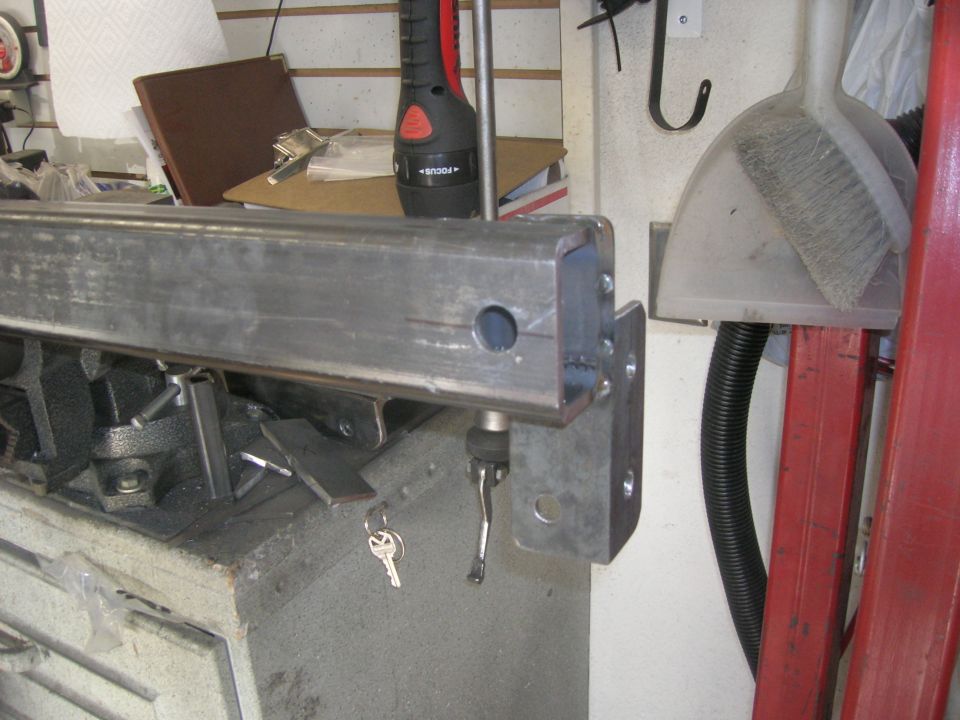 Metal bumper section with a hole drilled in it, held by a clamp, with keys hanging nearby