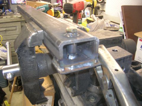 1996 Ford Bronco - A metal bracket is held in a vise, with a bolt and nut connecting it to a piece of tubing.