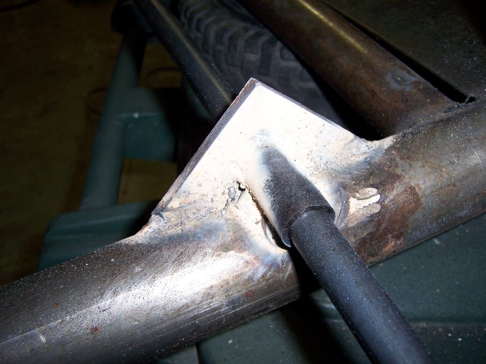 Welded bare-steel tube frame joint with triangular gusset plate on a workbench