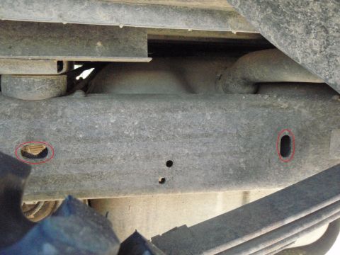 1995 Ford Bronco - Close-up view of the underside of a vehicle frame, showing suspension components and two marked holes.