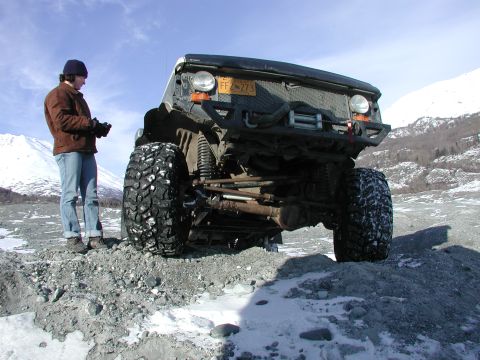 1990 Ford F-250 - A person stands next to a heavily modified truck with oversized tires in a snowy, rocky landscape.