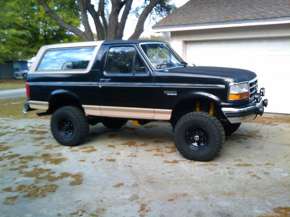 Black lifted Ford Bronco with tan lower trim parked by a garage