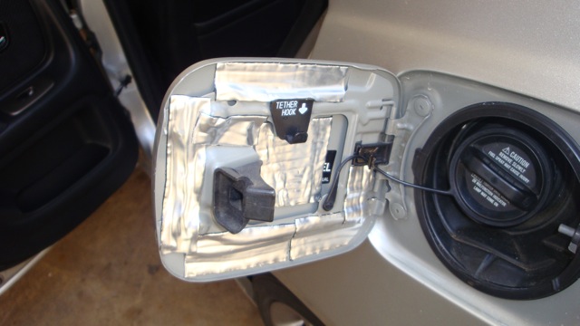 Open fuel door lined with foil sound deadener beside black fuel cap