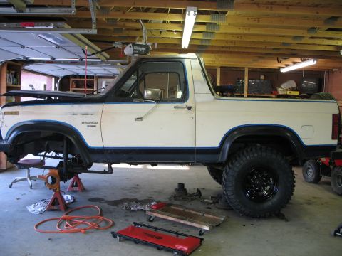 1985 Ford Bronco - Side view of a 1985 Ford Bronco being worked on in a garage, with tools and parts visible.