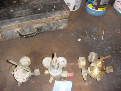 1992 Ford Bronco - Three welding-type gas pressure regulators with dual gauges laid out on a garage floor beside a metal tool box.