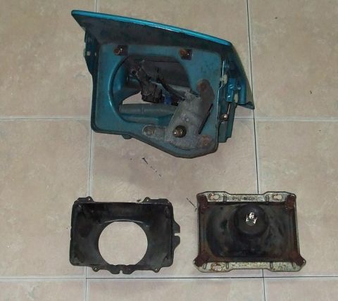 1994 Ford Probe - Disassembled car headlight assembly, including housing, bracket, and reflector, laid out on a tiled surface.