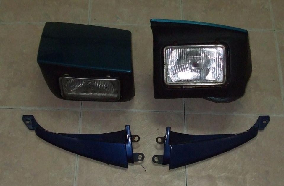 Two car headlights and two blue trim pieces are laid out on a tiled floor