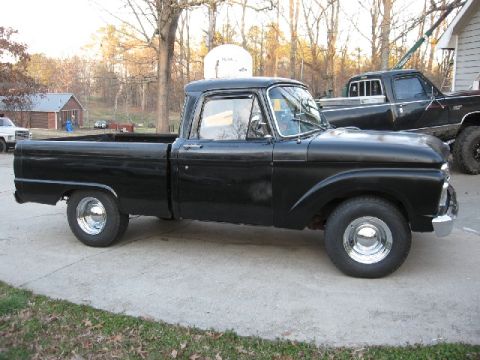 1966 Ford F-100 - A black 1965 Ford F-100 pickup truck is parked on a concrete driveway next to another truck.