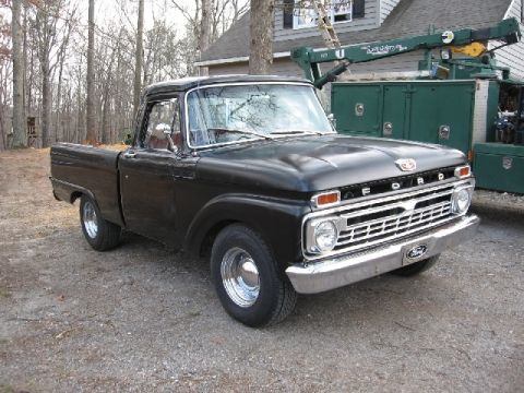 1966 Ford F-100 - This black 1966 Ford F-100 pickup truck is shown from a front 3/4 angle, highlighting its distinctive chrome grille.