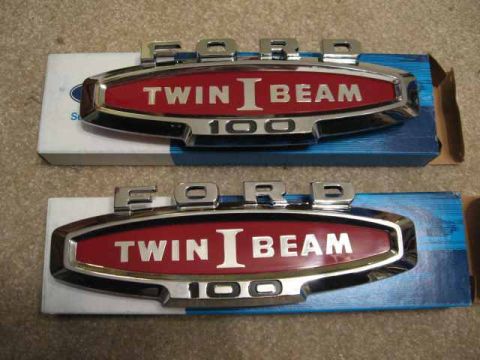 1966 Ford F-100 - Two Ford Twin Beam 100 emblems are shown, each with red inserts and chrome trim.