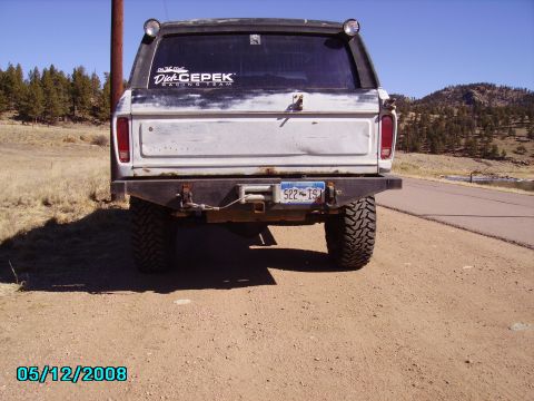 1978 Ford Bronco - Rear view of a white 1978 Ford Bronco with a custom bumper and off-road tires parked on a dirt road.