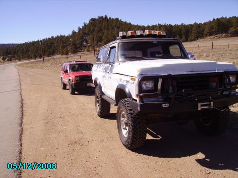 1978 Ford Bronco - Two SUVs, a 1978 Ford Bronco and a red Jeep Cherokee, are parked on a dirt road.