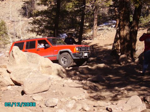 1978 Ford Bronco - A red Jeep Cherokee navigates a challenging, rocky off-road trail.