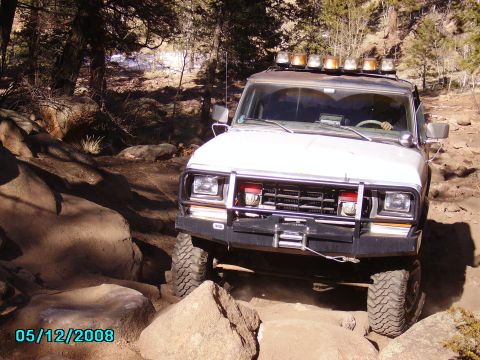 1978 Ford Bronco - White off-road SUV with roof lights navigating rocky terrain on a sunny day.