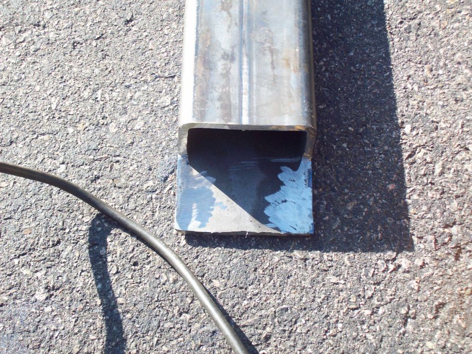 Square steel tubing on pavement with a primed end and a stray cable