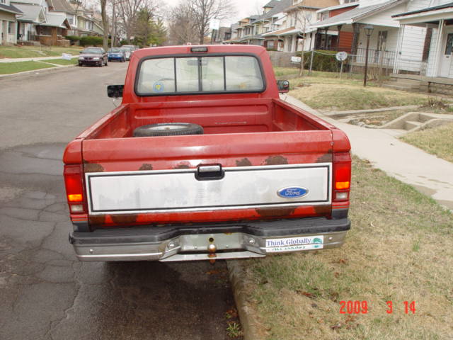 Rear of a red Ford pickup with tailgate up parked on a residential street