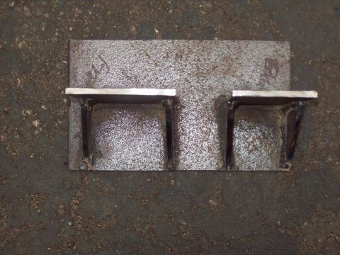 1989 Ford F-150 - A close-up, overhead view of a custom-made metal bracket with two small shelves welded onto a larger metal plate. The bracket is resting on…