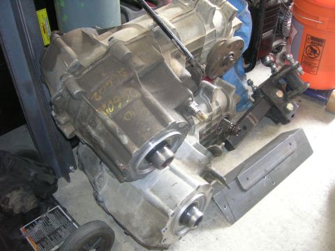 1996 Ford Bronco - A close-up, angled view of a transfer case assembly, likely from a 1996 Ford Bronco, is shown resting on a concrete floor. The transfer cas…