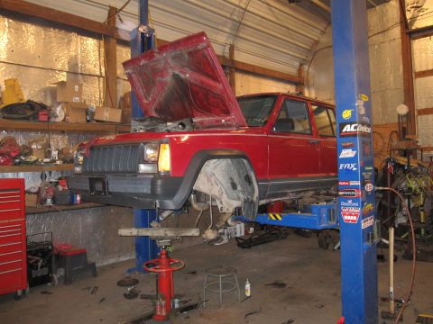 1992 Ford Bronco - Photograph of a red Jeep Cherokee on a lift with front suspension work underway, not a document.