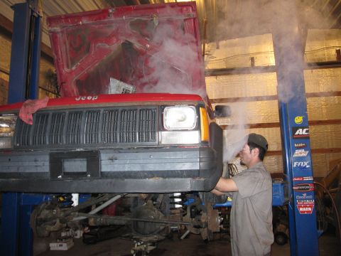 1992 Ford Bronco - Photograph of a technician working on a red Jeep raised on a lift, not a document.