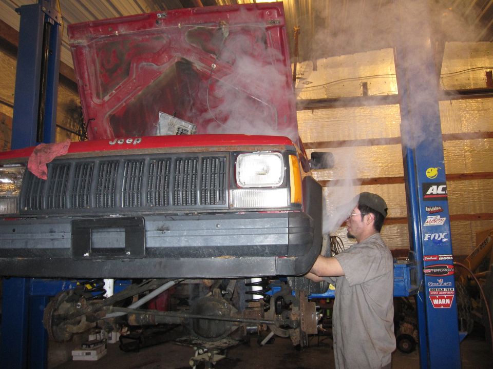 Photo of a person working under a red Jeep on a lift