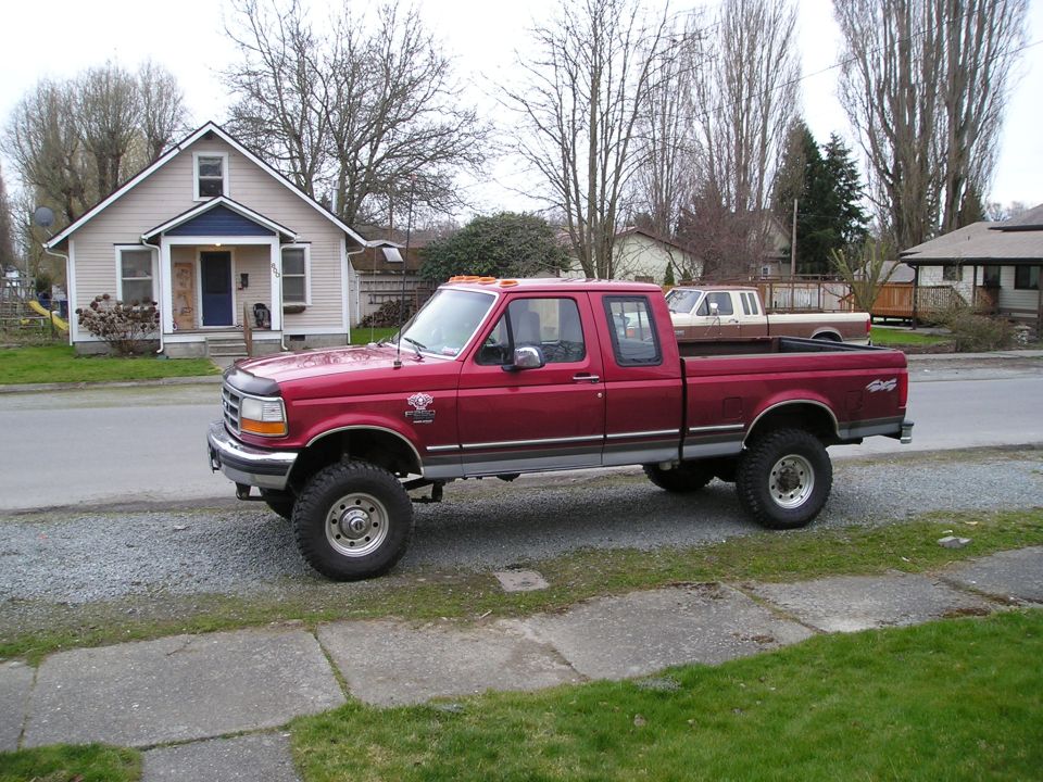 Red 1997 Ford F-250 pickup truck with large tires parked in front of a house.