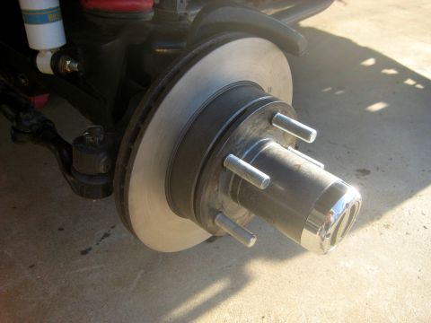 1996 Ford Bronco - A close-up view of the front passenger-side wheel hub and brake rotor assembly of a vehicle, likely a 1996 Ford Bronco, mounted on a concre…