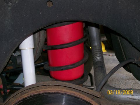 1995 Mercury Grand Marquis - A red air spring is visible between the coil spring and the vehicle's fender well, next to a white shock absorber. A portion of a rusty bra…