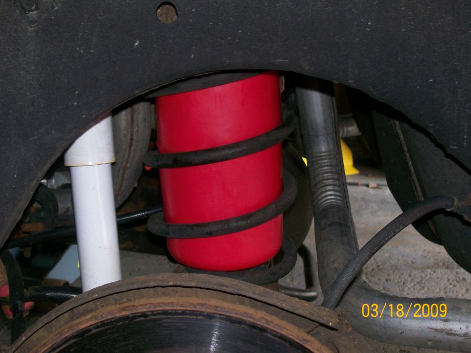 Red air spring and white shock absorber on a 1995 Mercury Grand Marquis rear suspension.