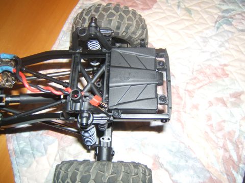 1988 Ford Bronco - Close-up view of the suspension and electronics of an RC rock crawler, showing the chassis, shocks, wiring, and a battery/electronics box.