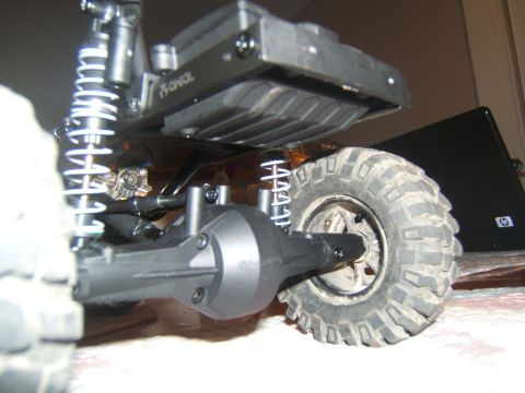 1988 Ford Bronco - A close-up, low-angle shot shows the rear suspension and wheel of a remote-controlled rock crawler. The vehicle features a black chassis, s…