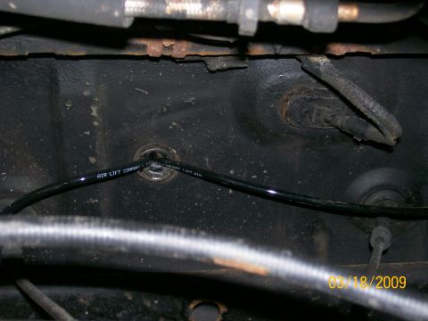 1995 Mercury Grand Marquis - A black air line labeled "AIR LIFT COMPANY" runs through a grommet in a dark, textured surface, likely the undercarriage of a vehicle. A ti…