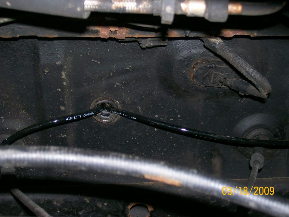 Black air line labeled AIR LIFT COMPANY going through a grommet on a dark vehicle surface.