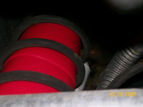 1995 Mercury Grand Marquis - Two red cylindrical parts with black rubber bands are visible, likely suspension components, next to a corrugated gray hose and some rusty…