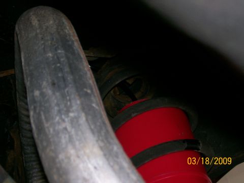 1995 Mercury Grand Marquis - A close-up view of a red suspension component with black bands, possibly an air spring or bump stop, is visible underneath a vehicle. A lar…