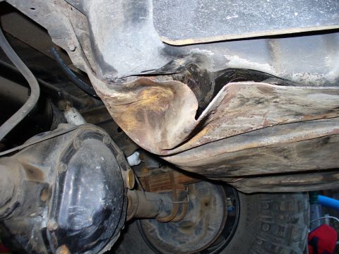 1978 Ford Bronco - The underside of a vehicle shows significant damage and rust to the fuel tank or a similar component, with a differential and part of a tir…