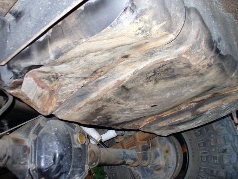 1978 Ford Bronco - Underside view of a vehicle's fuel tank and rear axle assembly, showing signs of rust and wear. The fuel tank appears to be a large, rectan…
