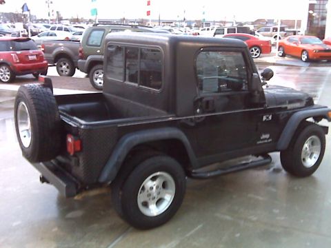2008 Jeep Wrangler - The rear driver's side of a black Jeep Wrangler pickup conversion is shown parked on a wet asphalt lot. A spare tire is mounted on the rear…